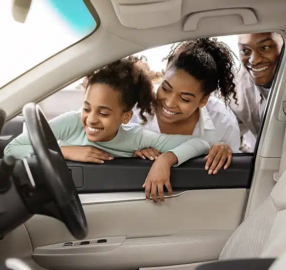 Family of three buying a new car, looking through window at auto interior