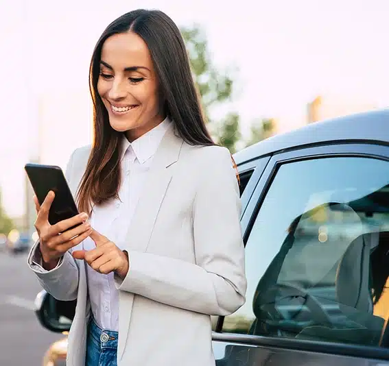 Woman in formal smart wear is using her smart phone while standing near modern car