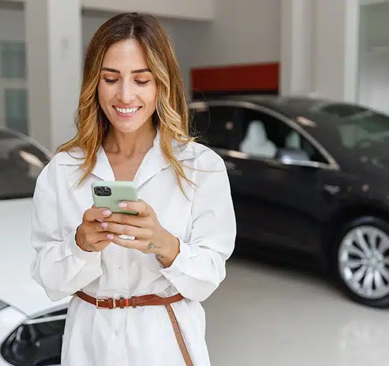 A woman in a new car showroom is using a mobile phone to quickly calculate an estimate of car loan repayments with a balloon payment added.