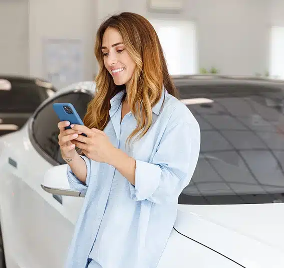 Woman using her mobile phone in a new car showroom to quickly estimate her car hire purchase repayments with Jade Finance.