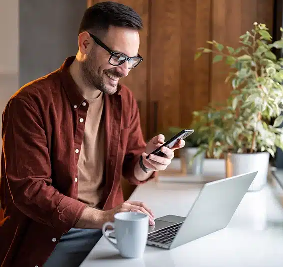 Man uses his smartphone and laptop to review the best self employed business loan repayments with Jade Finance.