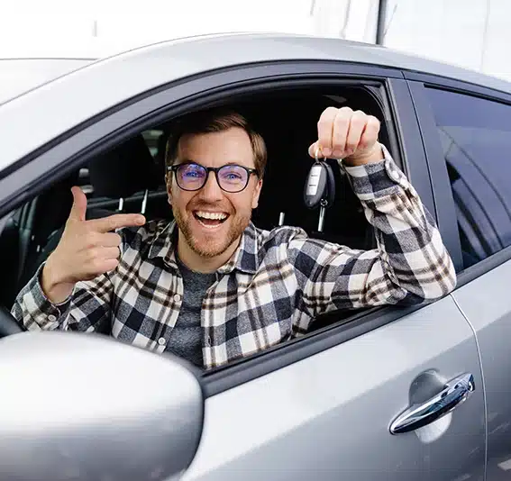 A man with glasses in a car is holding and pointing at a car key