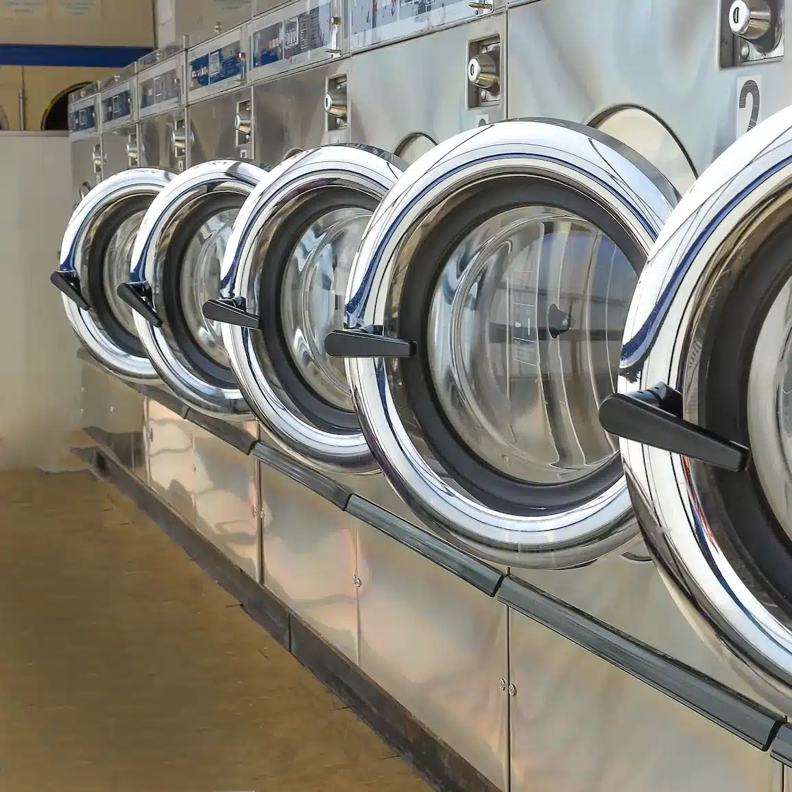 A row of industrial laundry washing machines with the doors open