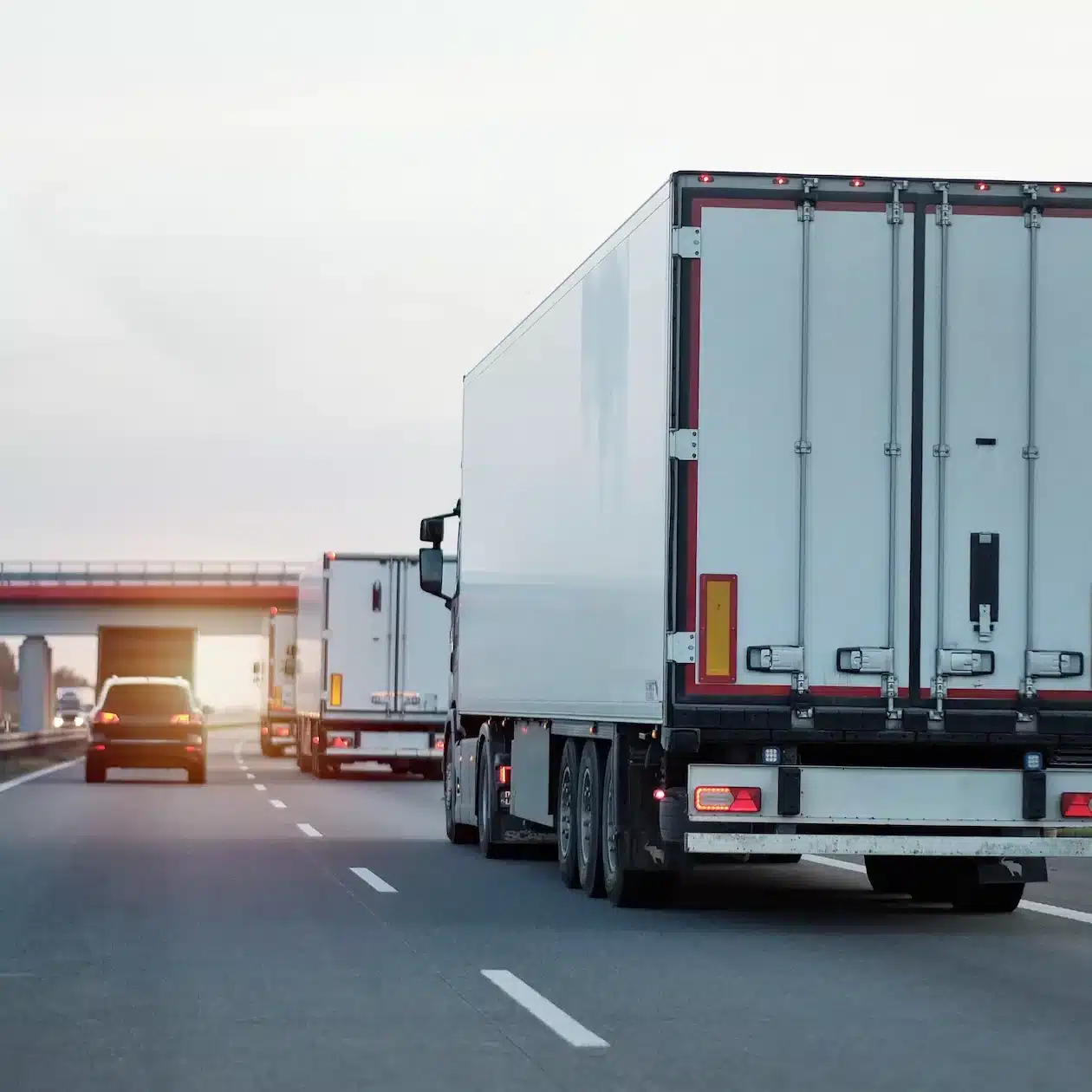 A few trucks driving away down the highway during sunrise
