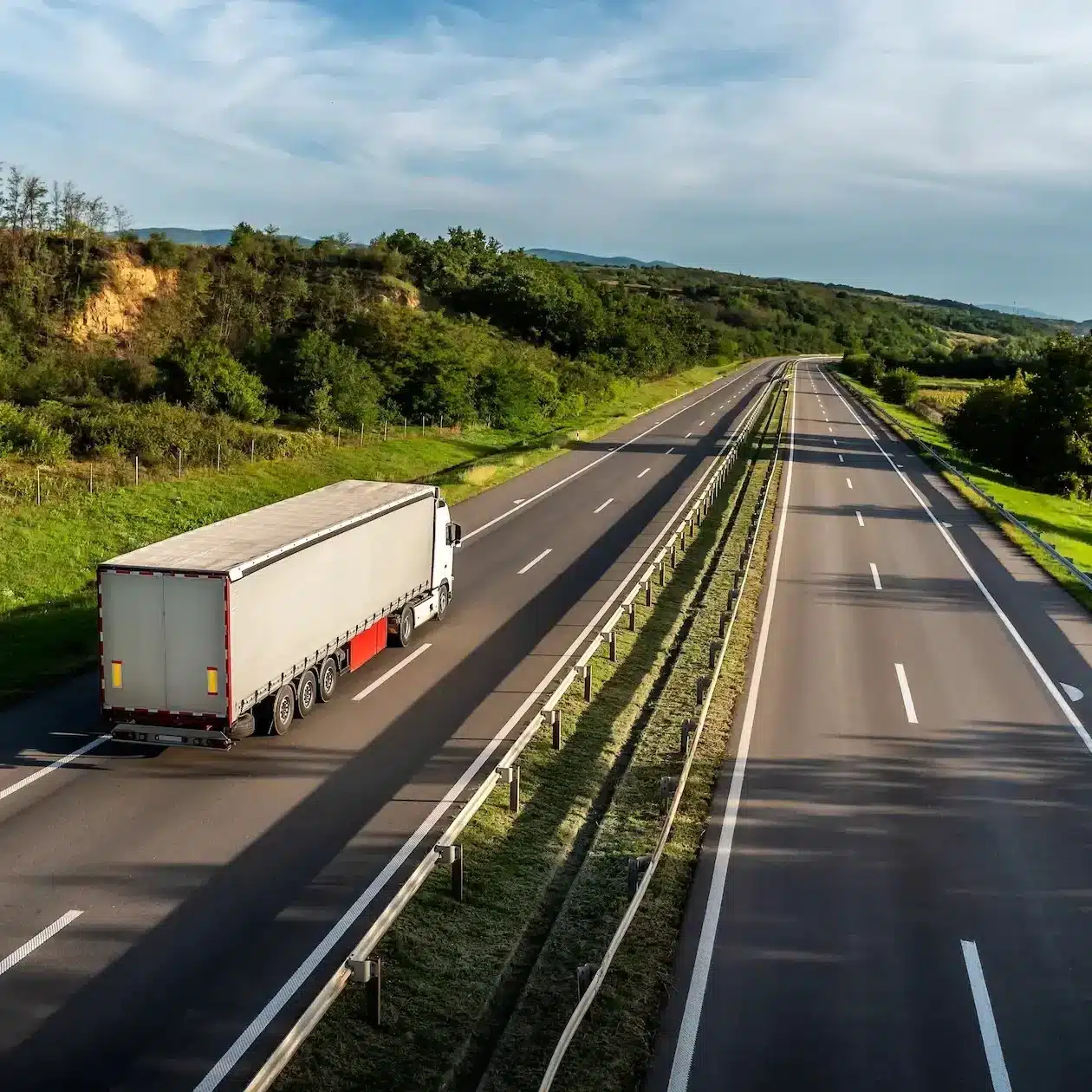 A truck with a large solid side trailer hauling freight down a highway through the green rolling countryside