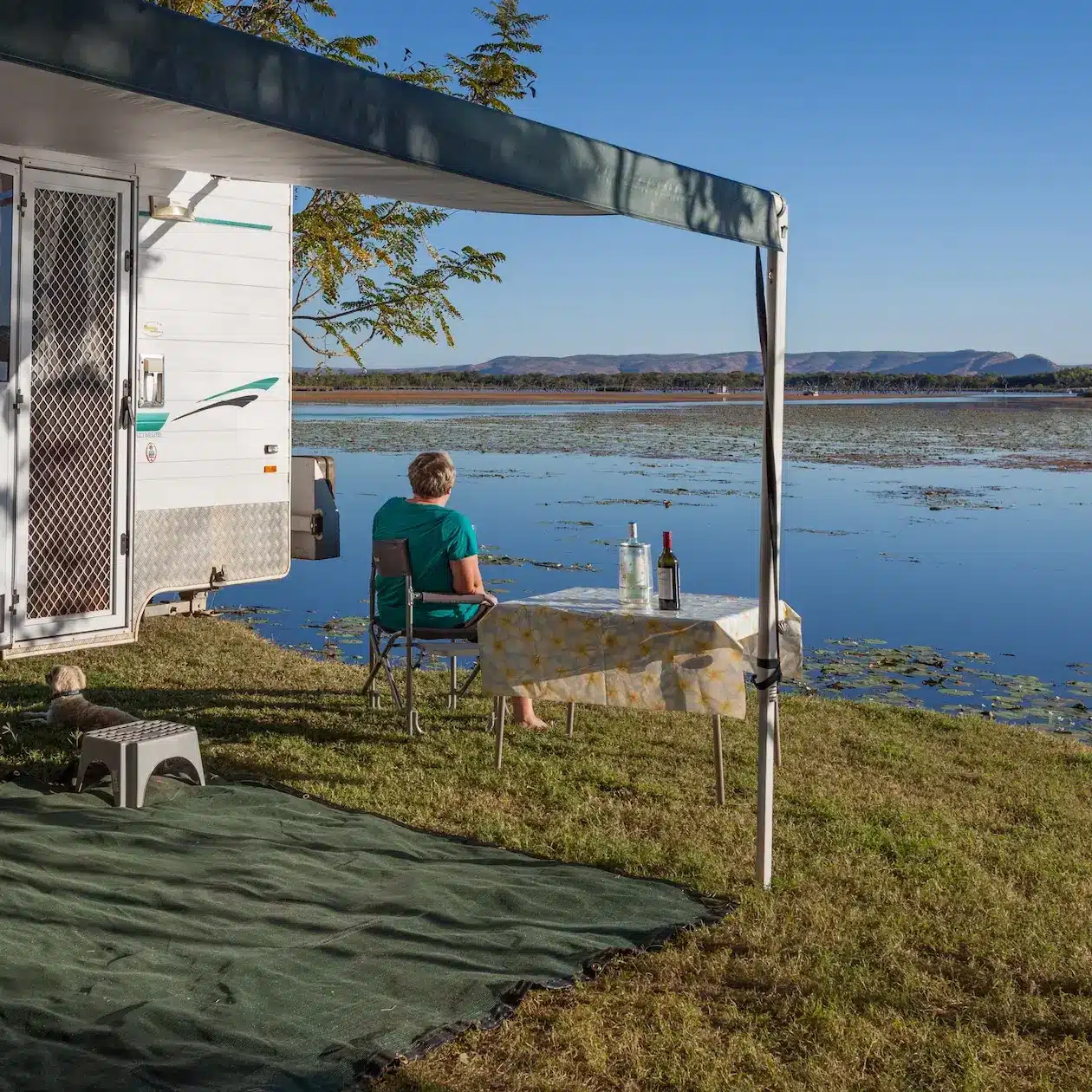 A lady sits under her used caravan awning taking in the view over the lake