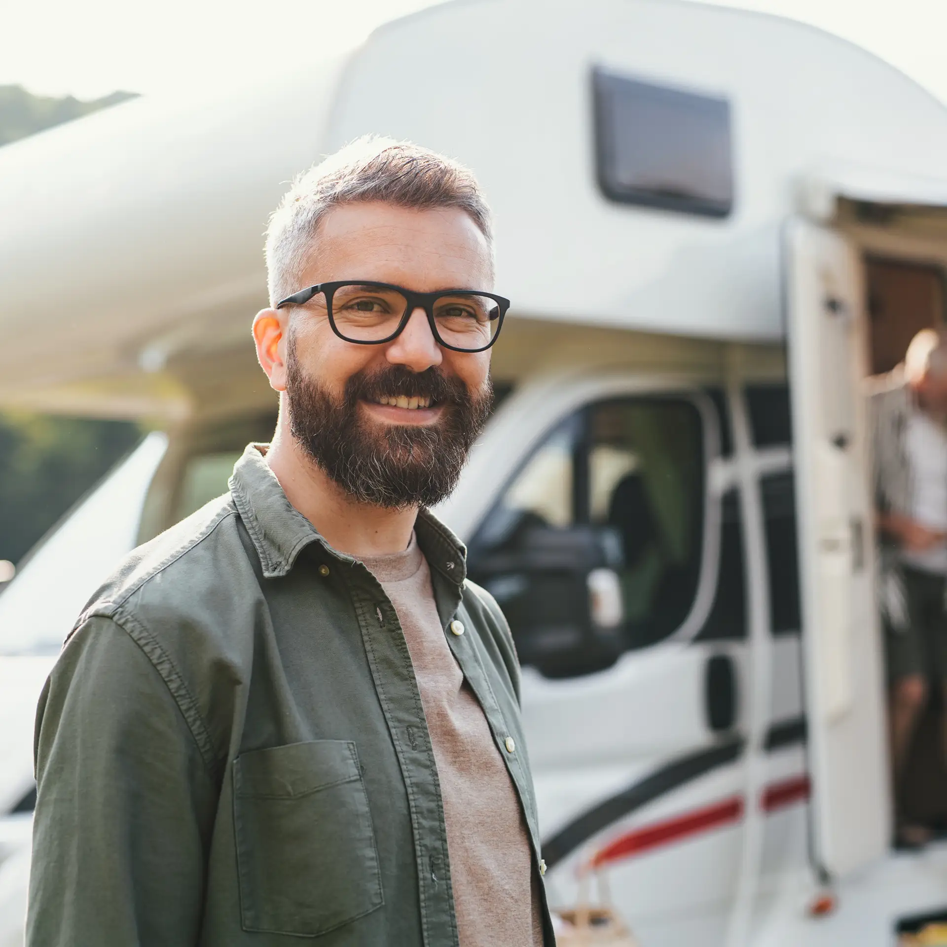 A happy man standing beside a caravan at a campsite outdoors