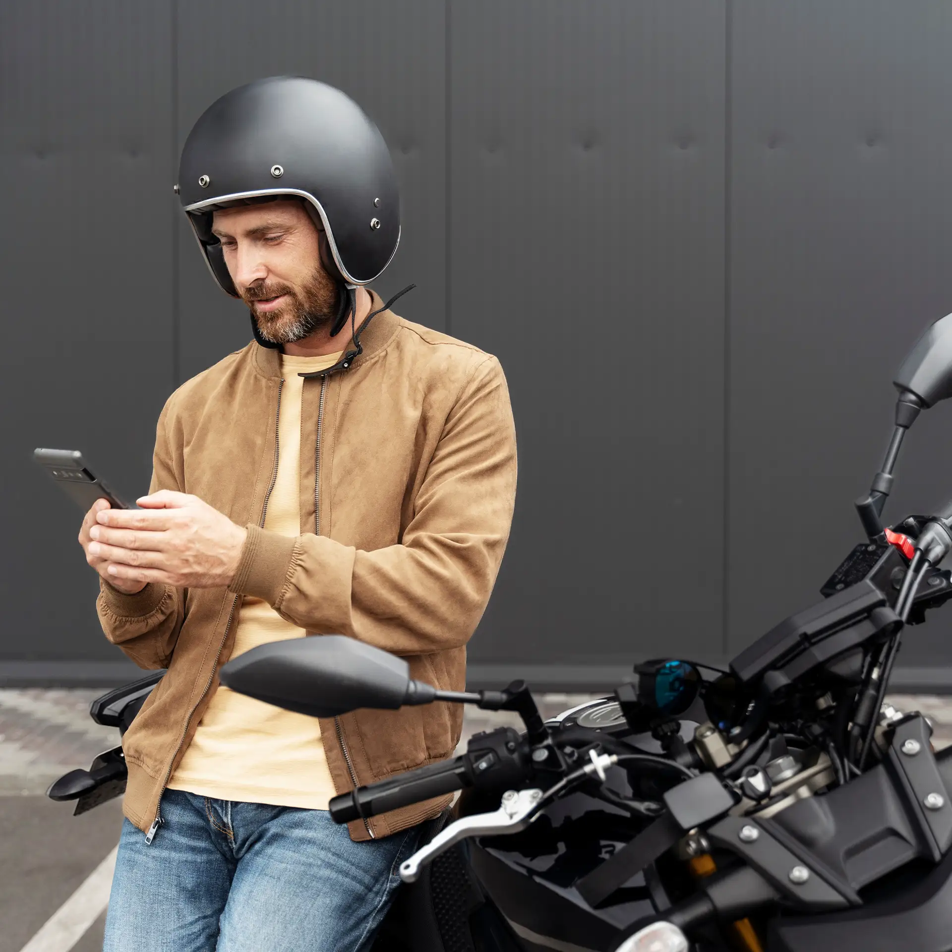 Biker leaning against his bike on his phone, using the motorbike loan calculator to calculate the repayments if he refinances his bike loan with Jade Finance.