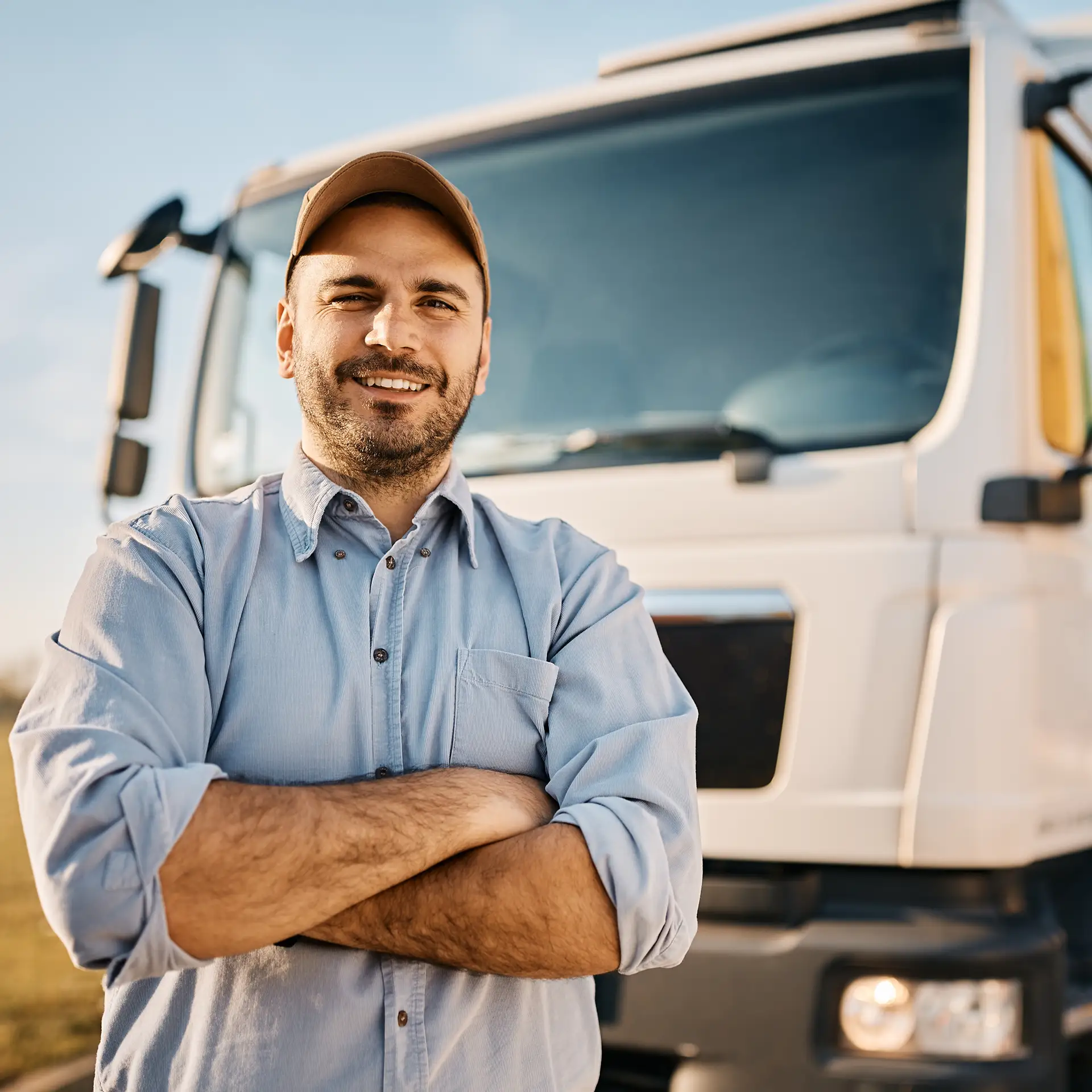 A smiling male driver standing in front of his truck