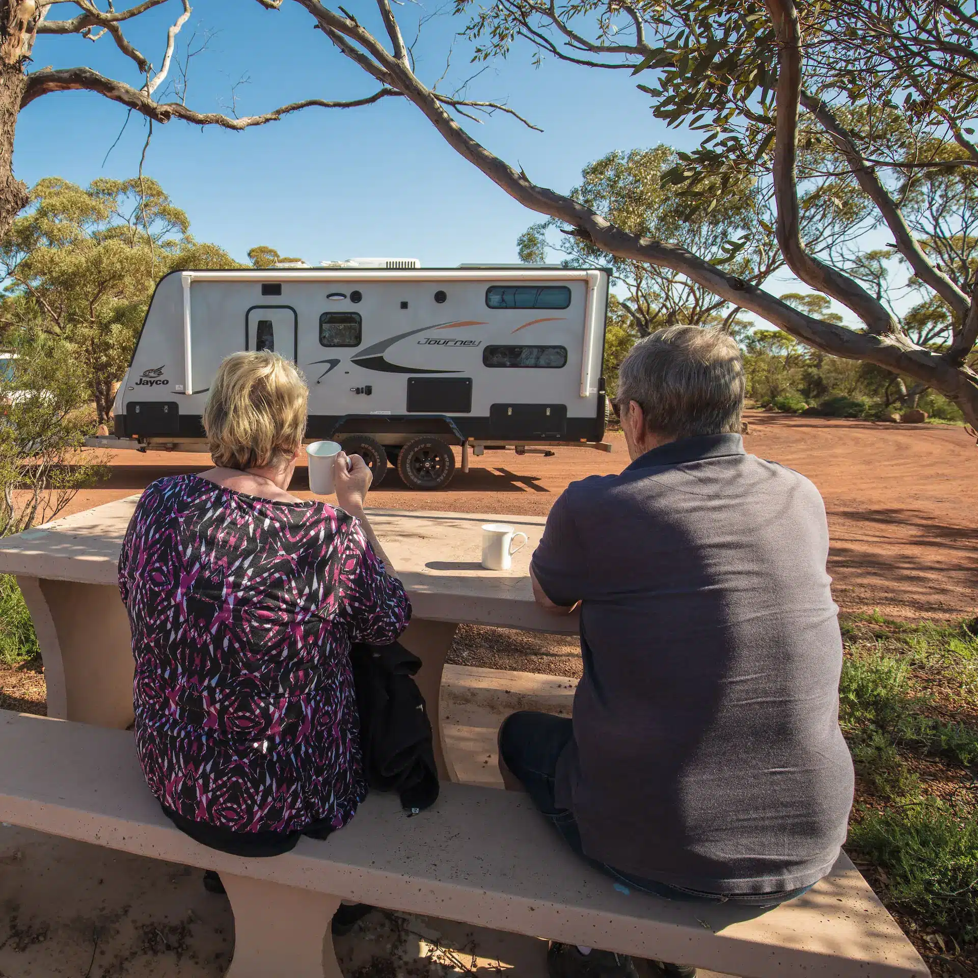 A retired couple touring Australia are sitting at a roadside stop, looking over at their caravan while thinking about upgrading through Jade Caravan Finance.