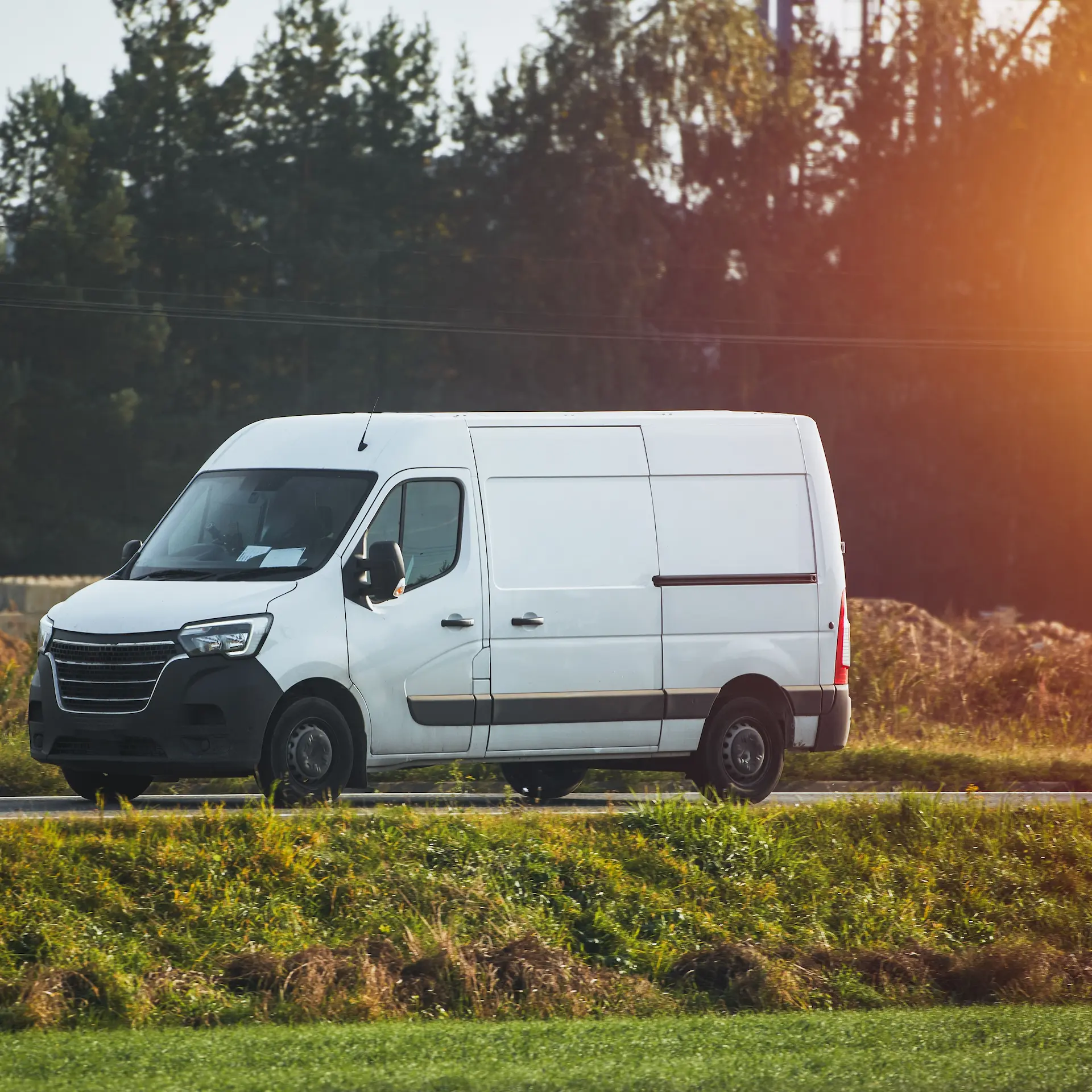 A commercial van driving along a country road while making deliveries.