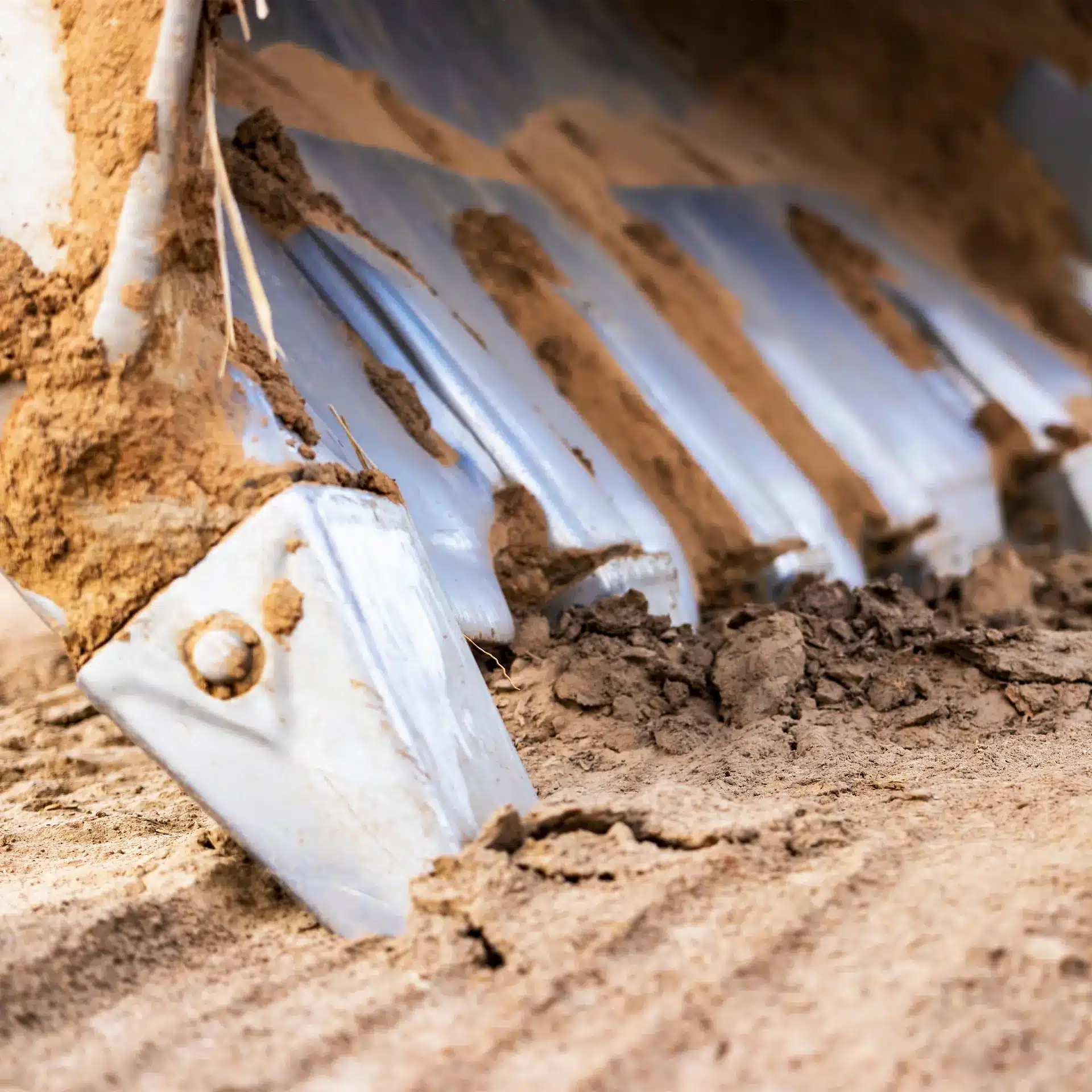 Close view of an excavator bucket beginning to dig in dirt, with the bucket teeth just breaking through the surface.