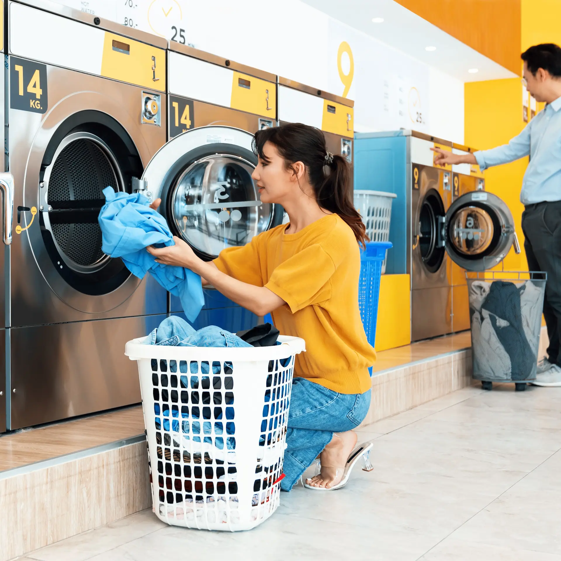 A lady is loading a commercial washing machine in a laundromat.