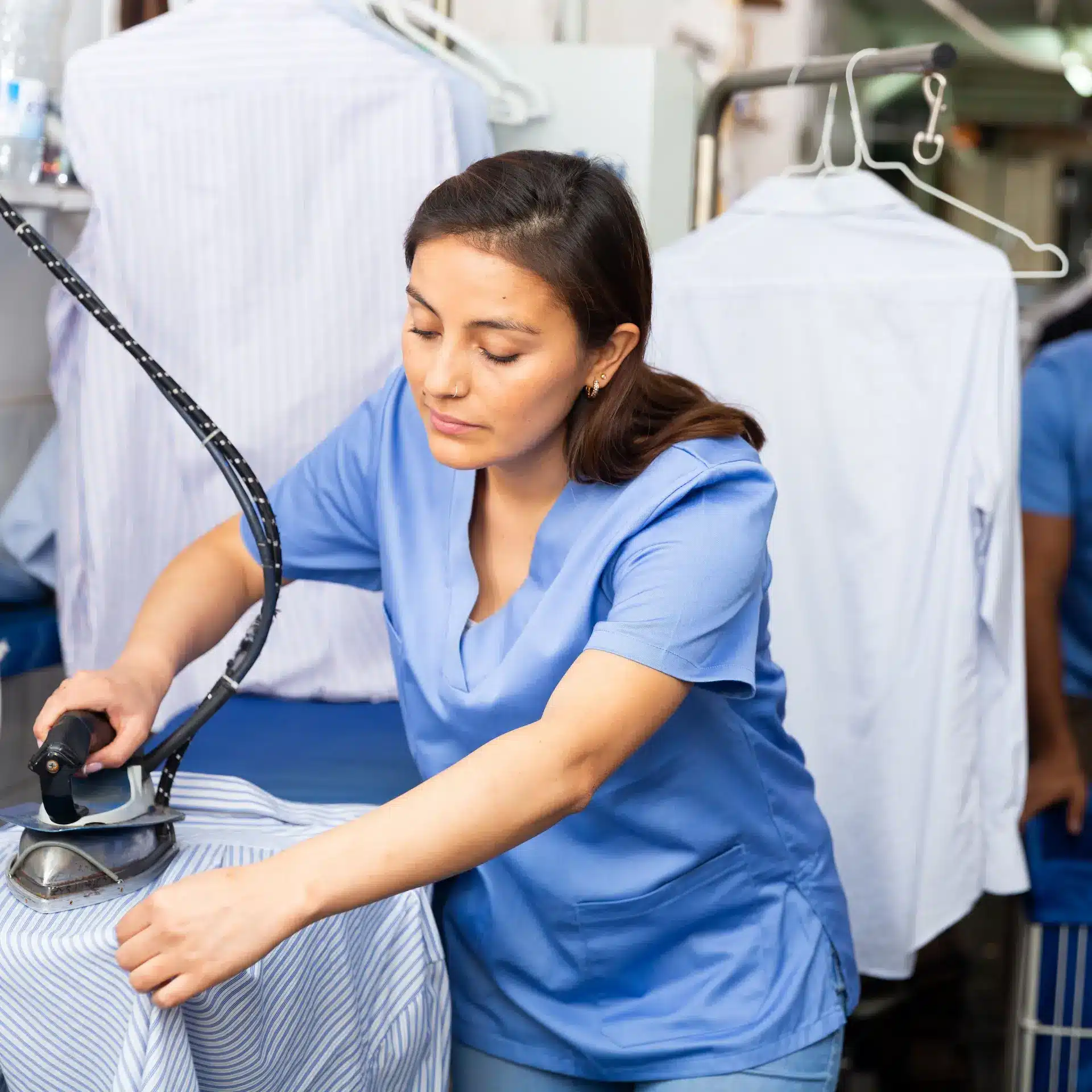 A professional laundry worker ironing customer garments using a steam iron.
