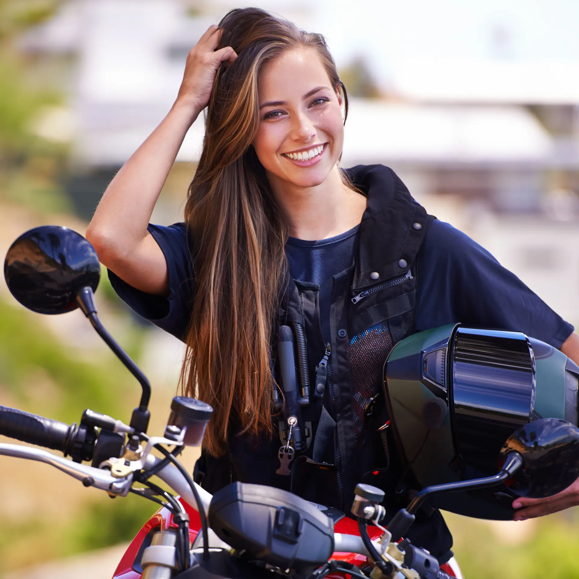 A young woman sitting on her parked motorbike fixing her hair after removing her helmet.