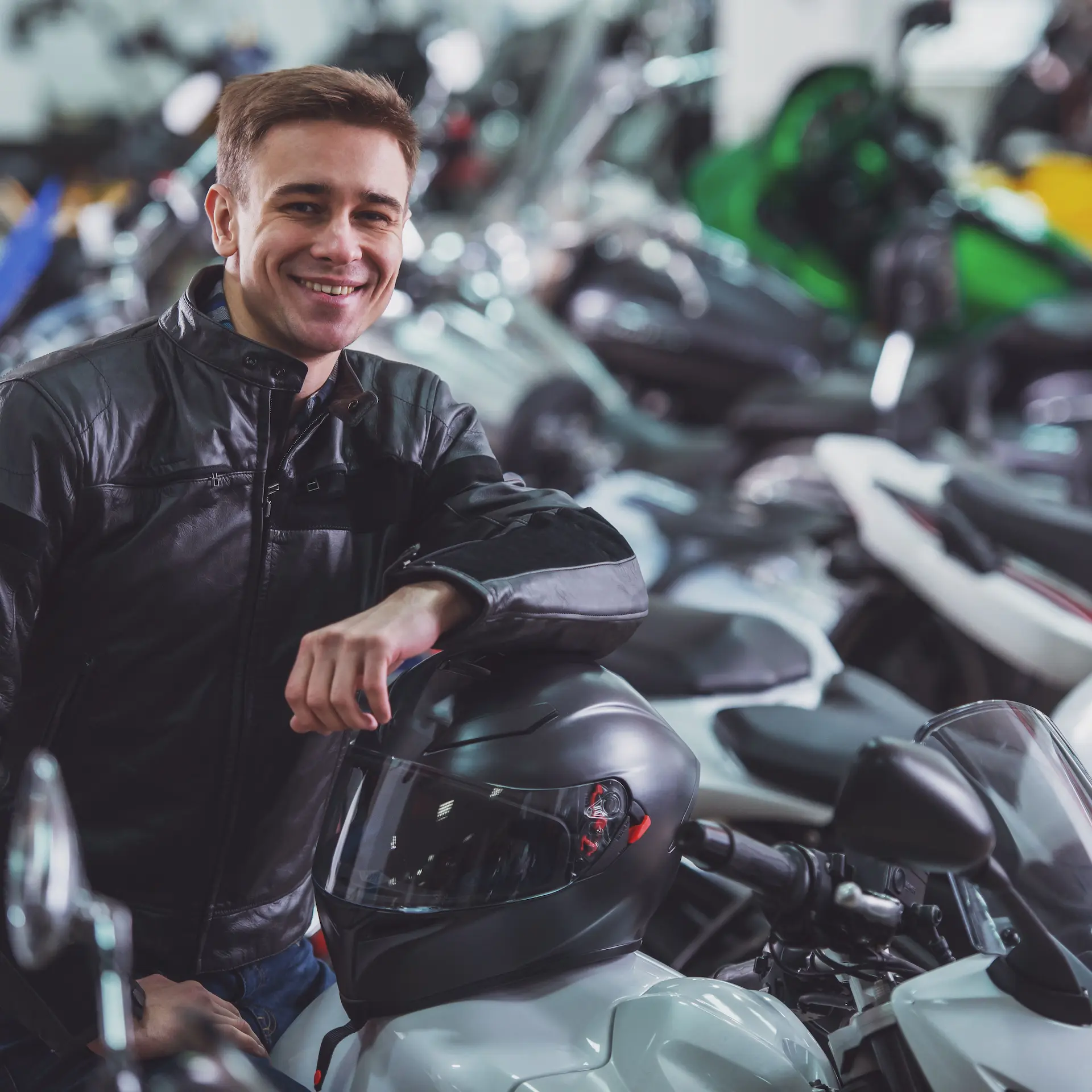 A young man sitting on a motorbike in a dealership showroom.