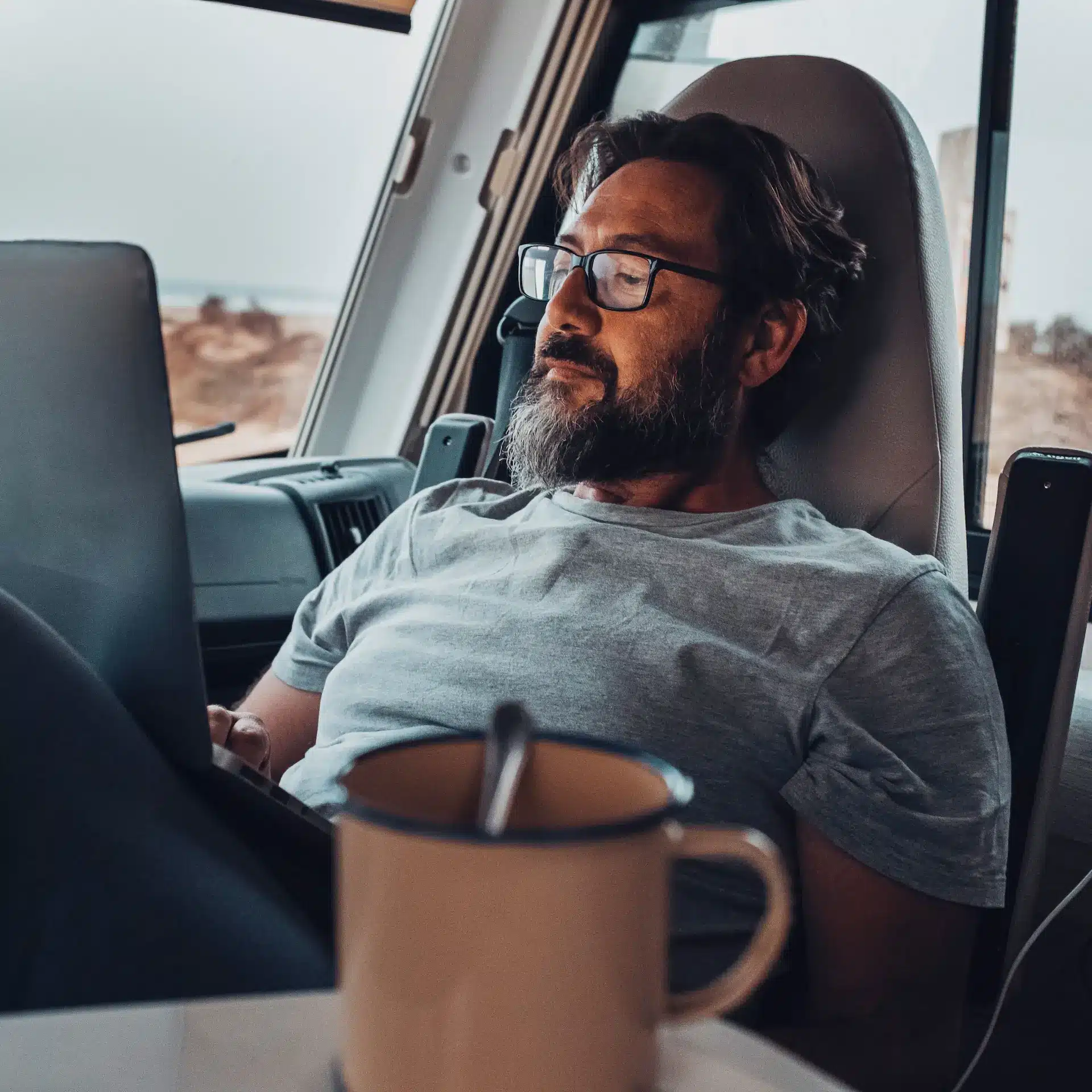 A man reclines in his seat in his RV with his laptop on his lap as he browses information about refinancing his RV to get better interest rates.