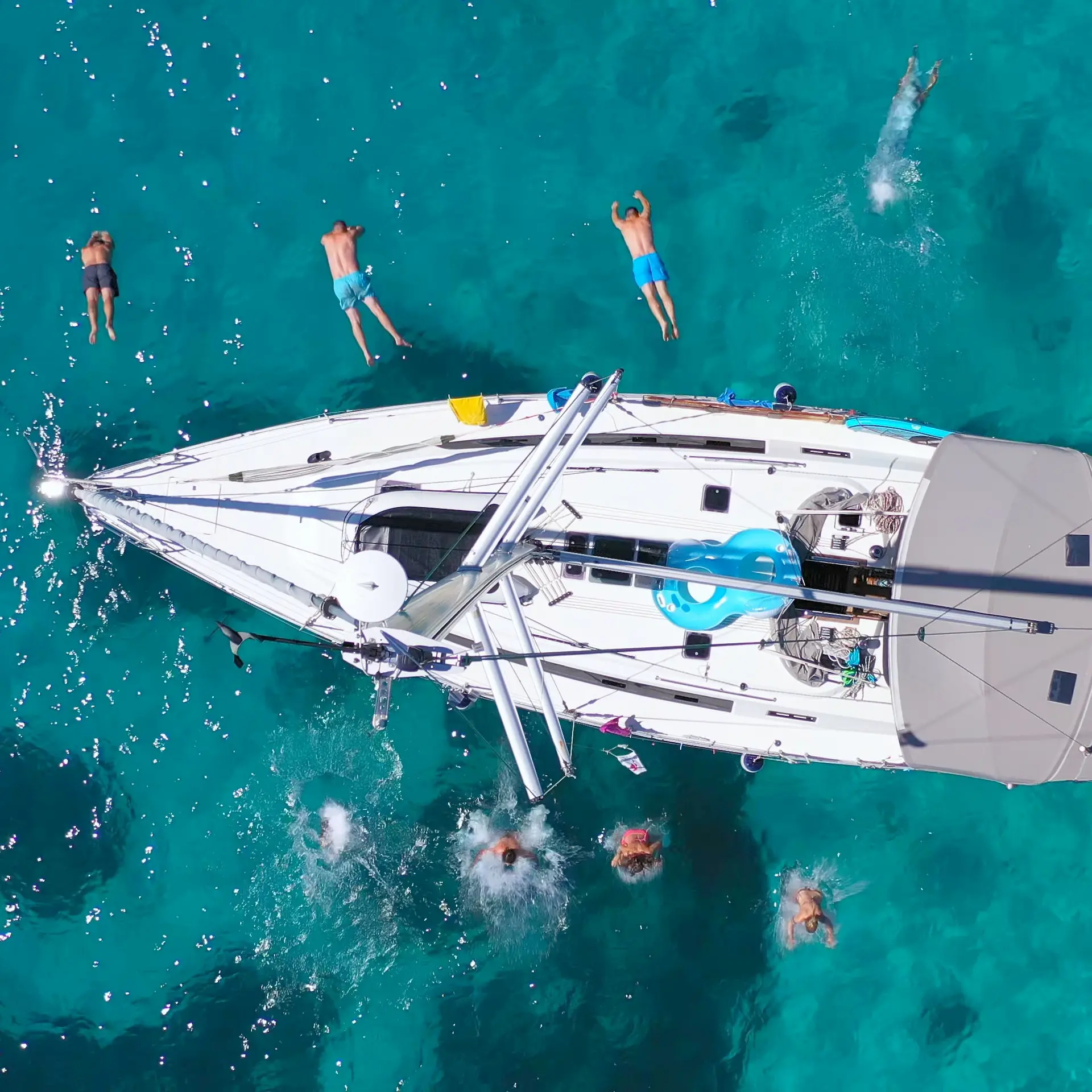 Top down arial view of a personal boat with several people snorkelling from it in clear blue waters.